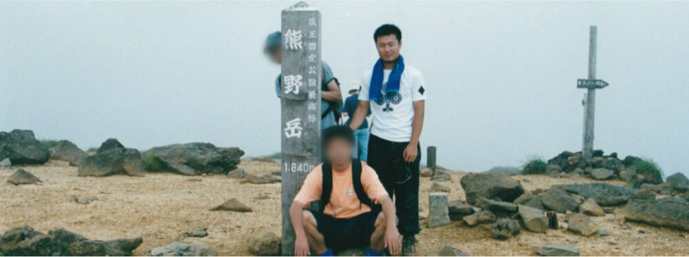 「熊野岳」と書かれた杭と、仲間たちと登頂記念撮影